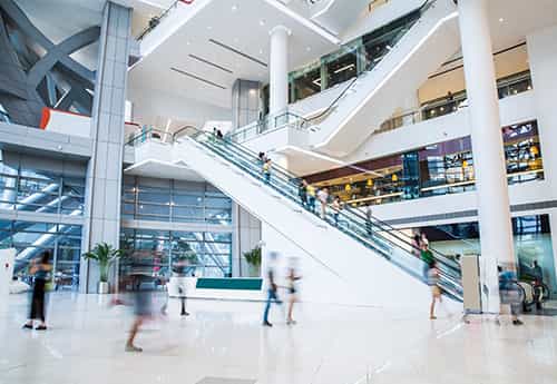 image of a mall atrium with escalators and consumers rushing about